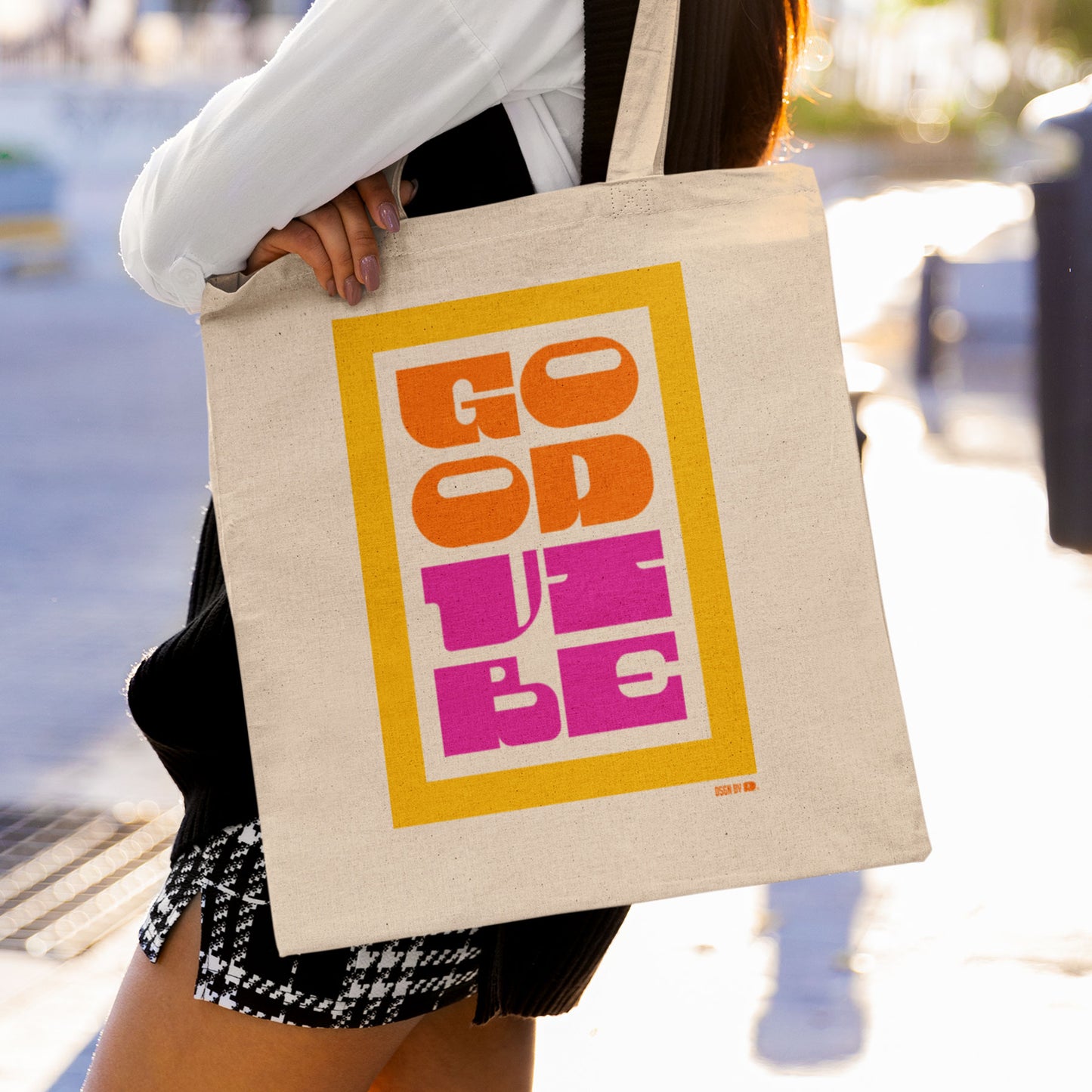 A woman carring cotton canvas tote bag with yellow, orange, and pink type showing "Good Vibe."
