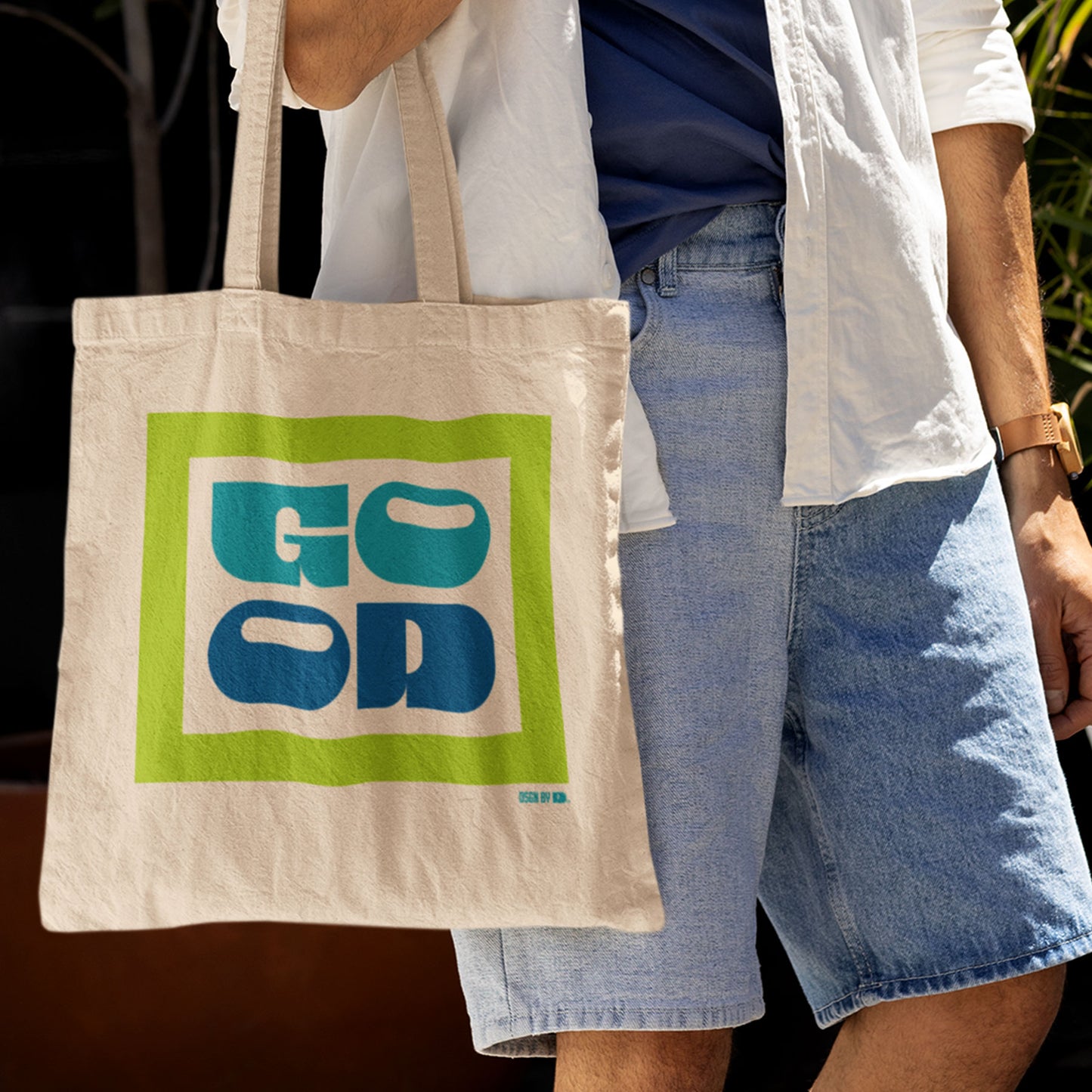 A man with a cotton canvas tote bag with green, teal, and bluek texts.