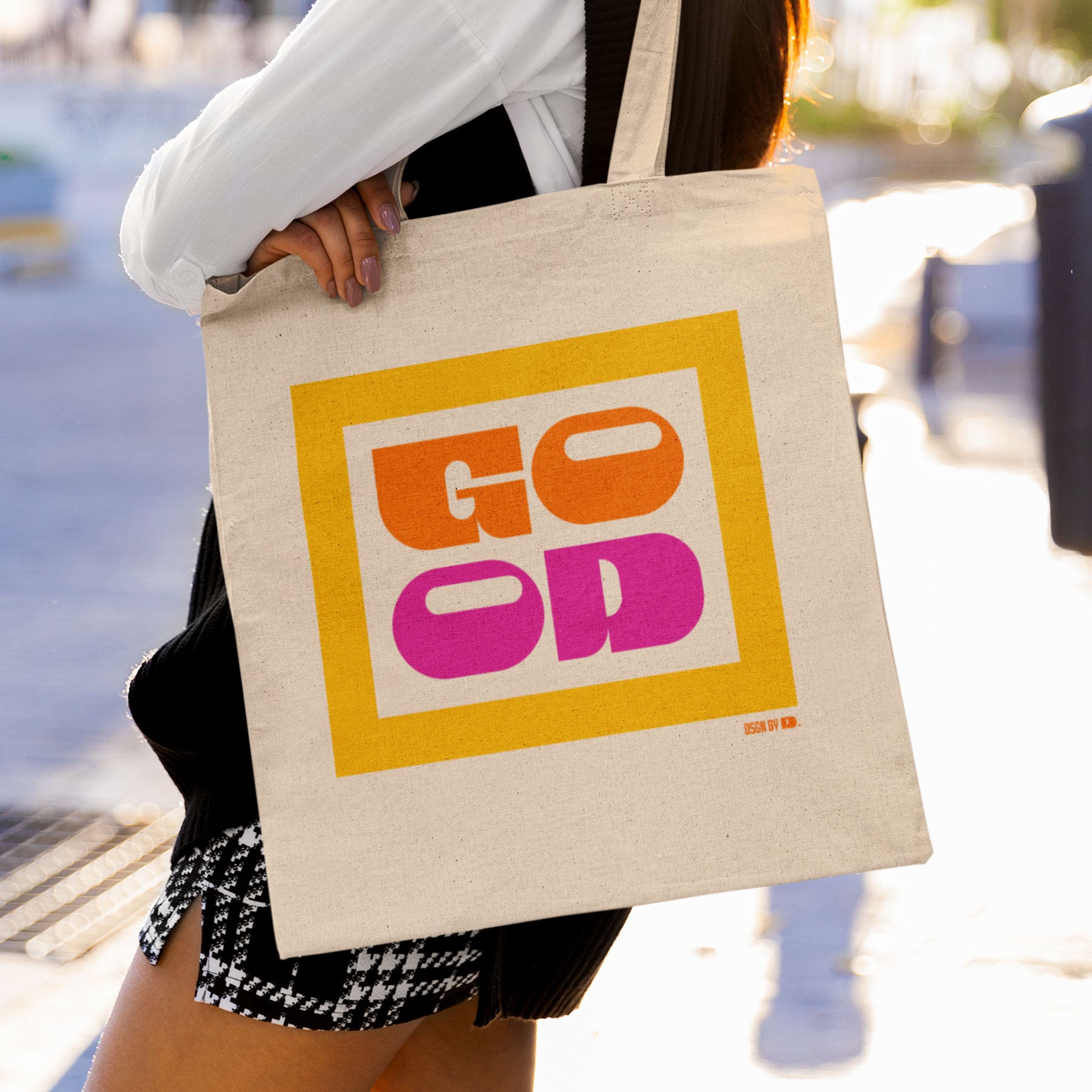 Woman carring a cotton canvas tote bag with yellow, orange, and pink texts.