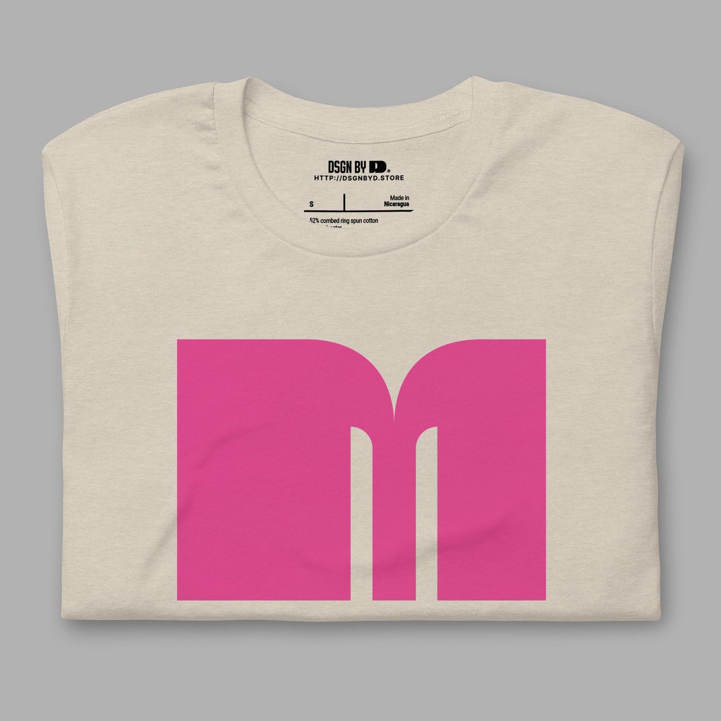 A folded beige cotton unisex graphic tee with letter M.